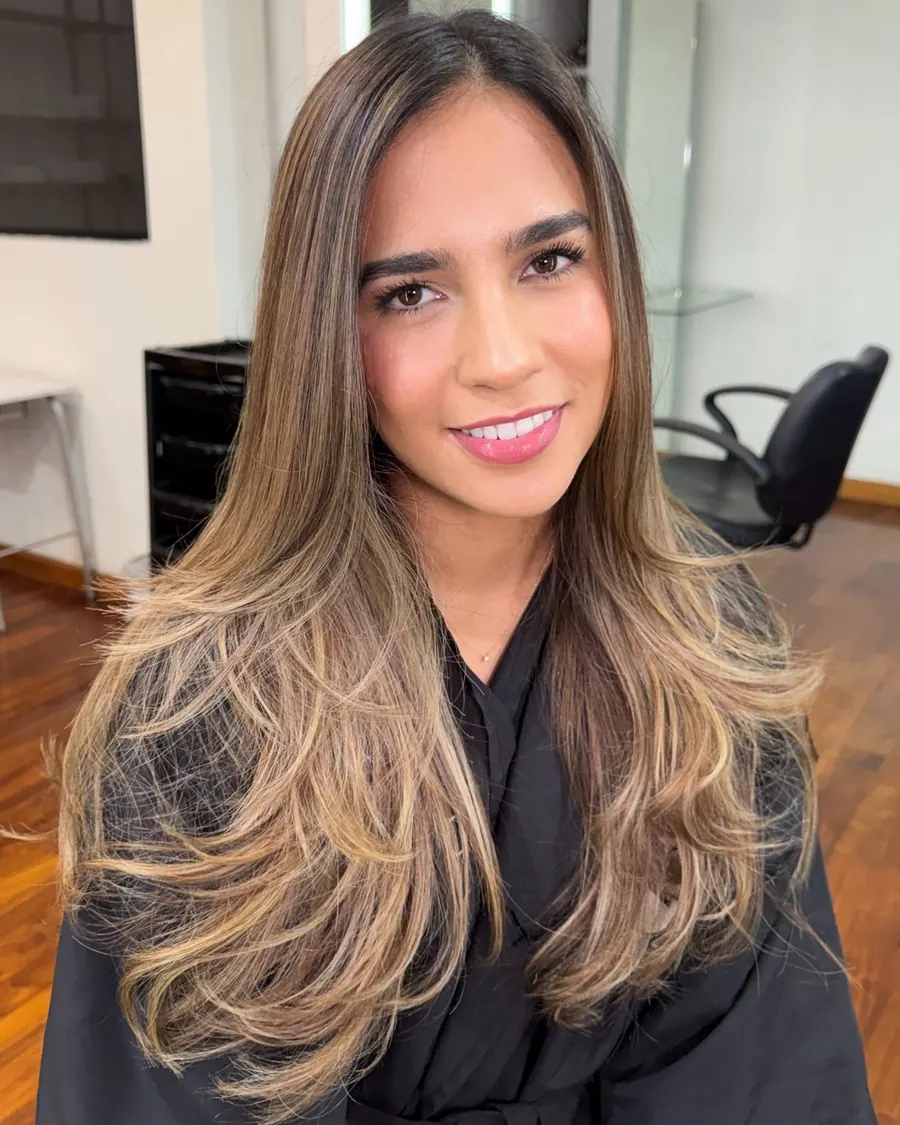 Clienta sonriente con balayage en tonos cocoa sobre base castaña, de frente en el salón