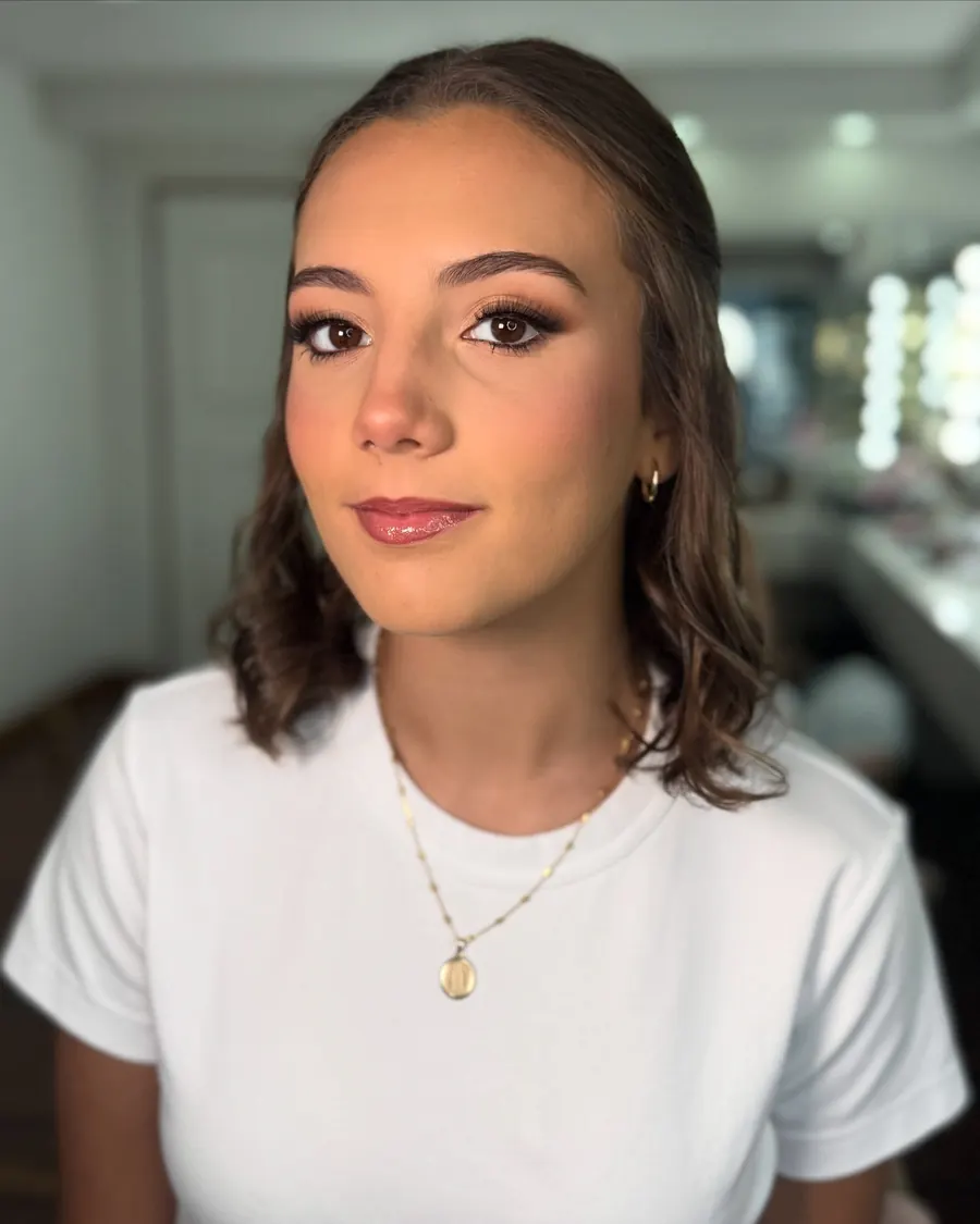 Clienta joven con ondas suaves y maquillaje luminoso, sentada en el salón